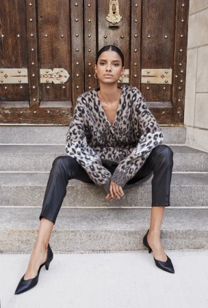 Woman sitting on stone steps wearing a leopard print sweater and black leather trousers against a wooden door.