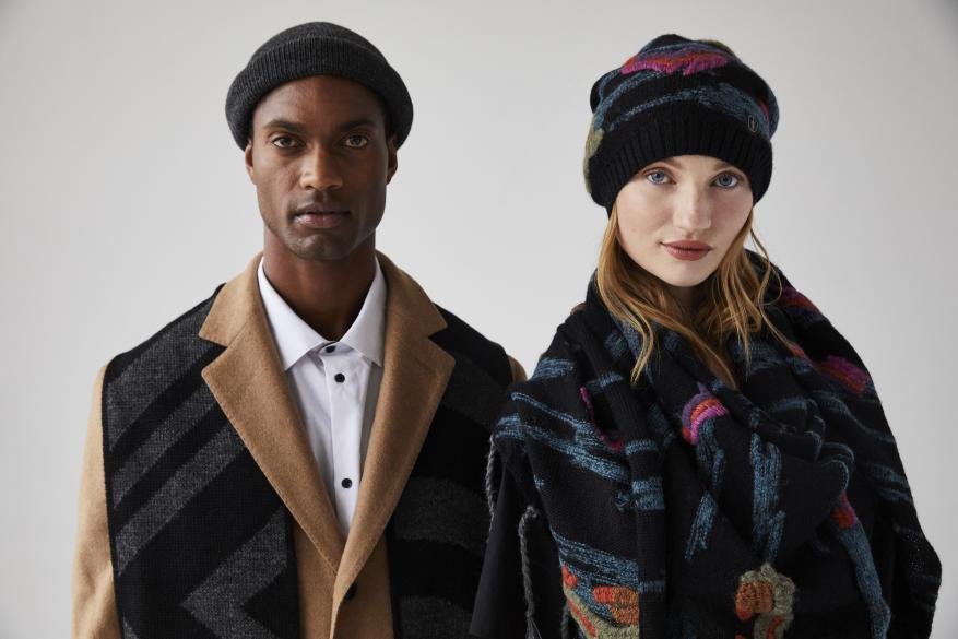 Fashion shot of an African American man and Caucasian woman wearing winter hats and scarves, posing in front of a neutral background.