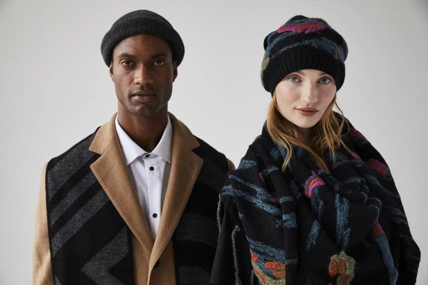 Fashion shot of an African American man and Caucasian woman wearing winter hats and scarves, posing in front of a neutral background.