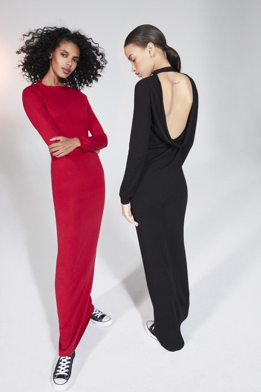 Two adult females wearing long-sleeve, full-length dresses, one red and one black, pose side-by-side in a studio wearing black and white sneakers.