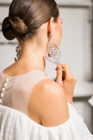Close-up of a model wearing large ornate crystal earrings and a white off-the-shoulder dress with a styled low hair bun