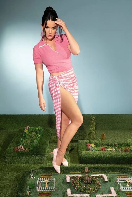 Full-length portrait of an adult female model with dark hair posing outdoors on a miniature landscape wearing a pink top and pink-and-white sarong.