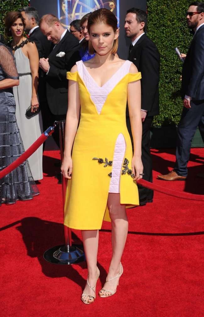 Kate Mara poses on the red carpet wearing a yellow dress with a thigh-high slit and strappy heels at a formal entertainment event.