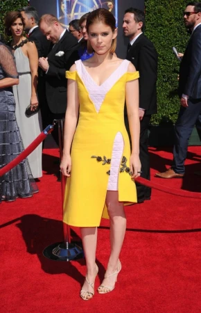 Kate Mara poses on the red carpet wearing a yellow dress with a thigh-high slit and strappy heels at a formal entertainment event.