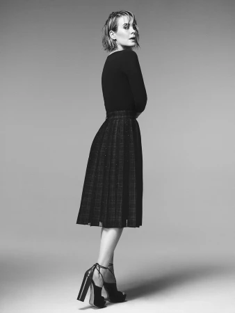 Portrait of a woman wearing a dark fitted top and pleated midi skirt with heeled sandals, styled by Johnny Wujek.