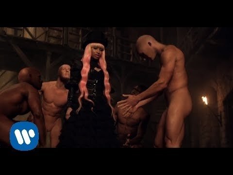 A woman in a black dress and hat stands surrounded by bare-chested men, set in a dark and mysterious setting with minimal lighting.