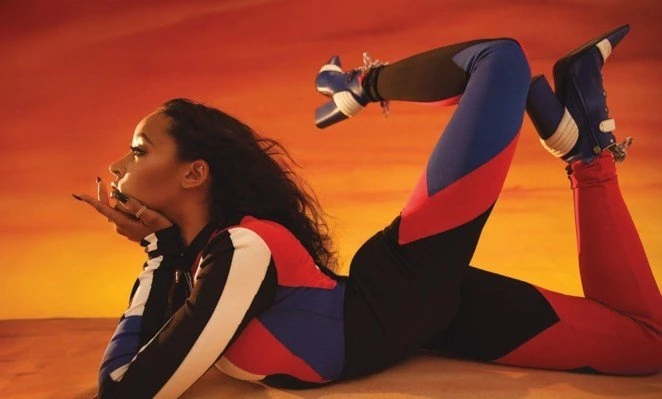 Woman in black, blue, and red sportswear poses in front of an orange and yellow background, showcasing athletic fashion and studio photography.