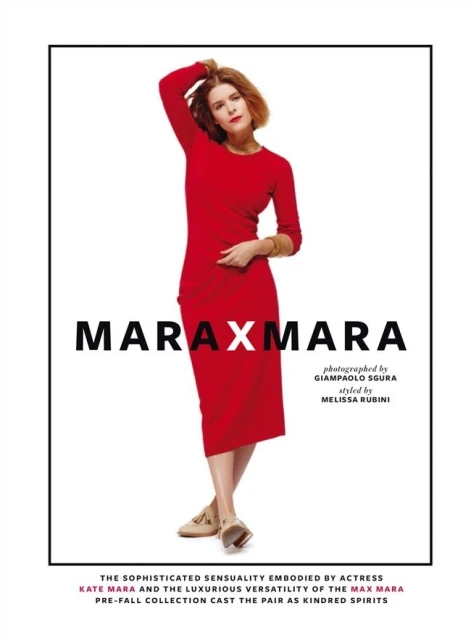 Kate Mara poses in a full-length studio shot. She is wearing a red dress and beige flats, standing in front of a white background.