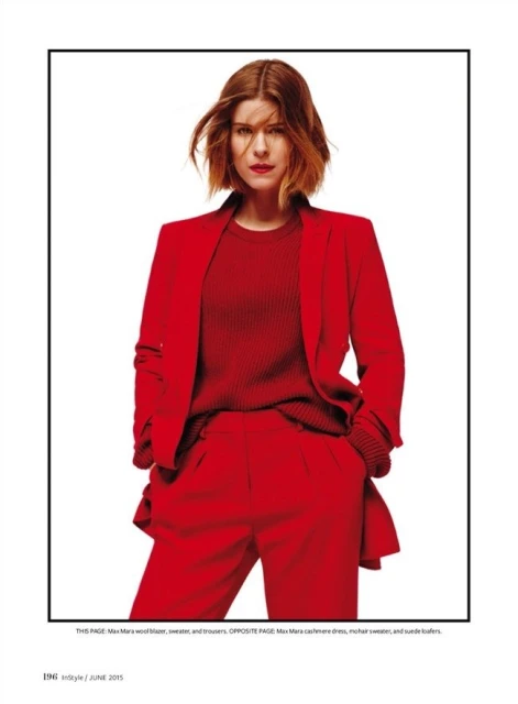 A woman with shoulder-length auburn hair poses in a red blazer, top, and trousers, set against a bright white backdrop in a studio.