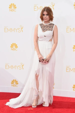Kate Mara poses in white gown on red carpet at the 66th Primetime Emmy Awards with NBC and Emmy logos in the background.
