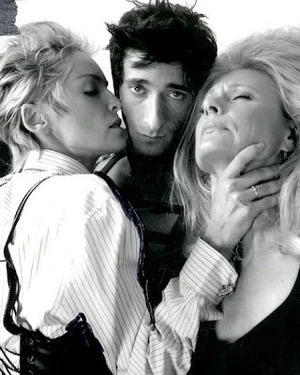 Black and white portrait of Adrien Brody posed tightly between two women in pinstriped shirts.