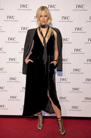 Blonde model in black velvet dress and strappy heels poses on a red carpet in front of an IWC Schaffhausen branded backdrop.