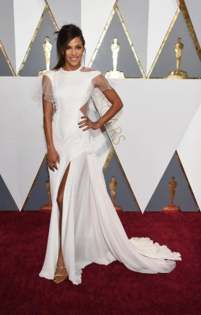 Woman in a long white evening gown standing on a red carpet against an Oscars step and repeat backdrop