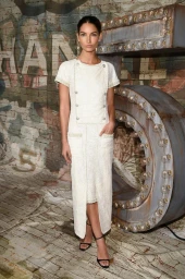 Model wearing a white tweed dress standing against a brick wall with large illuminated number sculpture styled by Jordan Foster
