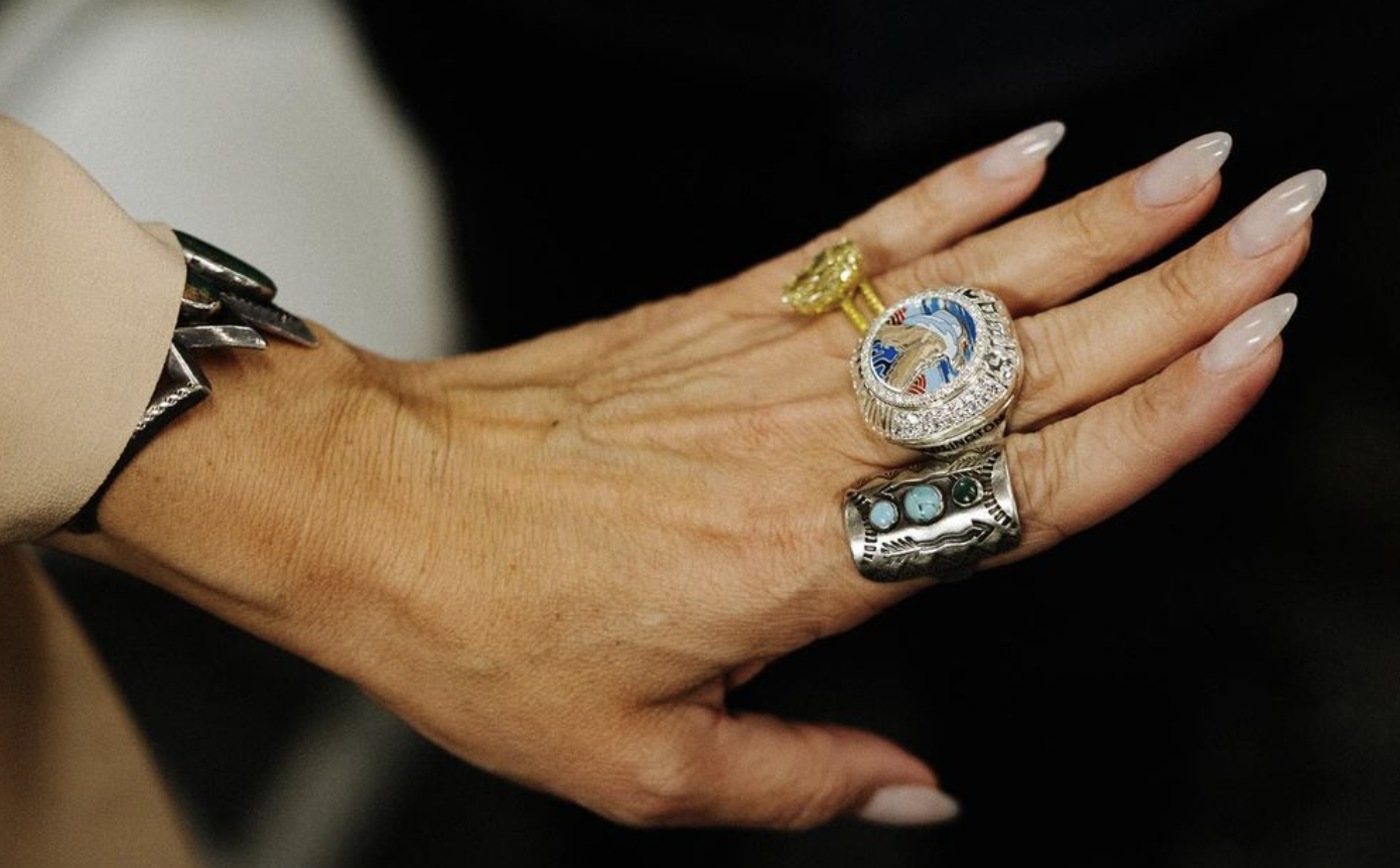 Close-up of an adult female hand adorned with statement rings and a metal bracelet against a dark background, emphasizing jewelry.