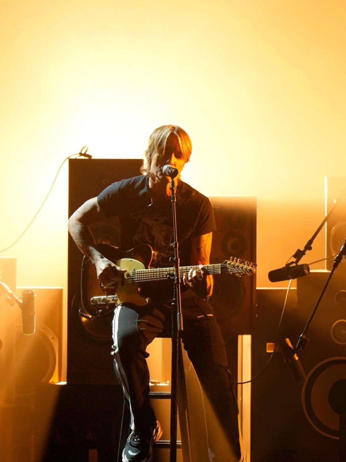 Man singing and playing guitar on stage with microphone and speakers in warm light in an indoor music venue performing live.