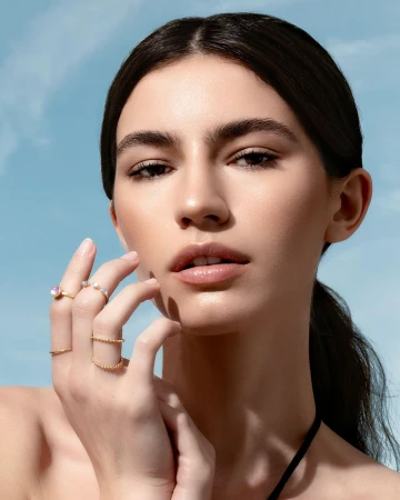 Close-up portrait of a woman wearing gold rings against a clear blue sky background