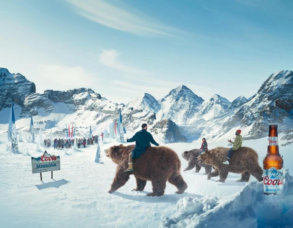 Coors Light advertisement in a snow-covered mountain range features people riding bears with snowy mountain peaks and branded signage.