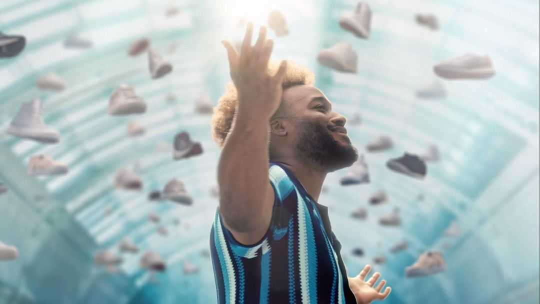 Man looking up surrounded by floating shoes in a light-filled space. He wears a blue striped shirt and has blonde hair.