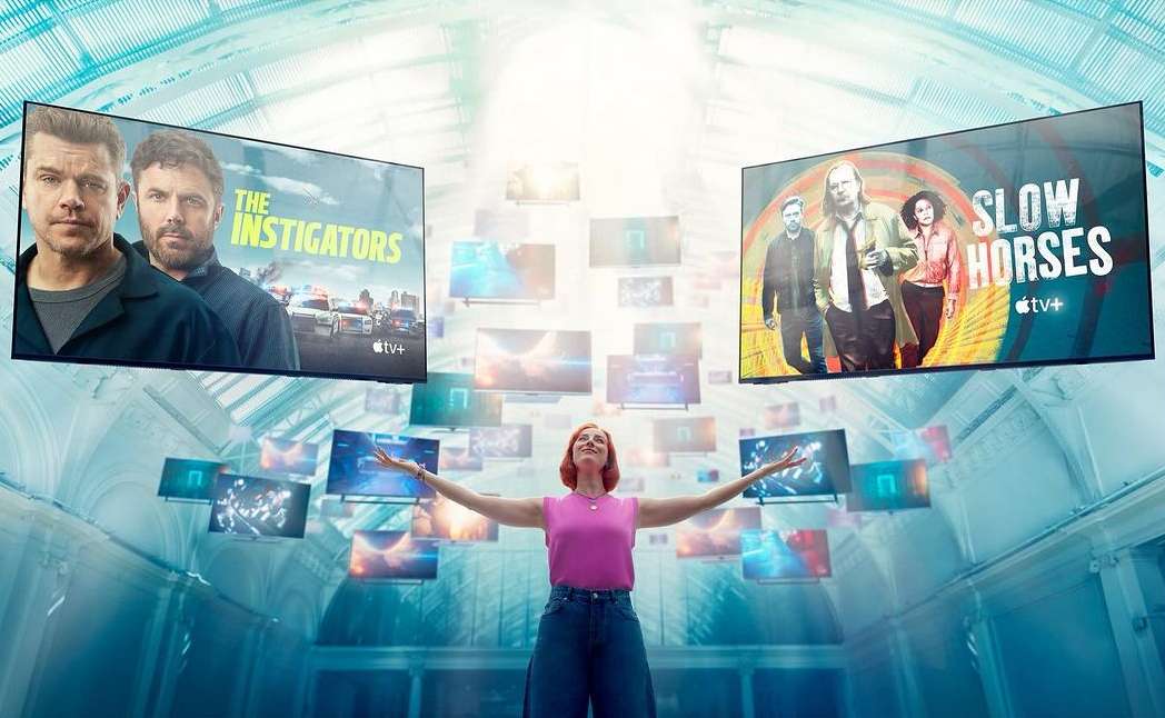 Woman with outstretched arms stands in a blue-toned hall surrounded by floating TVs showing movie posters in a promotional image.