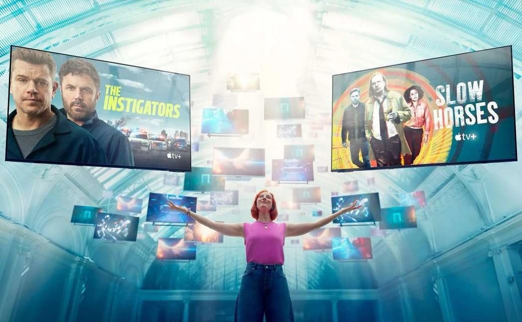 Woman with outstretched arms stands in a blue-toned hall surrounded by floating TVs showing movie posters in a promotional image.