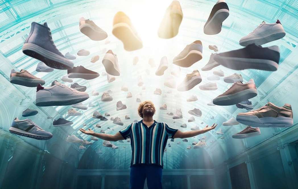 Man stands in an ornate hall with arms outstretched as many sneakers float around him in a bright, eye-catching conceptual shot.