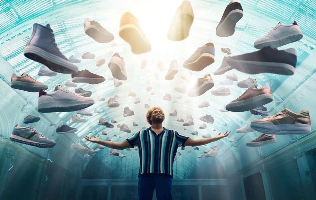 Man stands in an ornate hall with arms outstretched as many sneakers float around him in a bright, eye-catching conceptual shot.