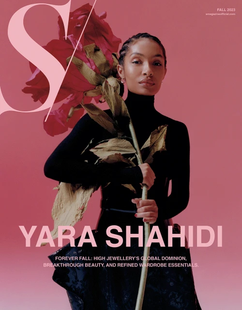 Yara Shahidi poses on a pink magazine cover with a large pink S and holds a dried rose in front of a black turtleneck top and skirt.