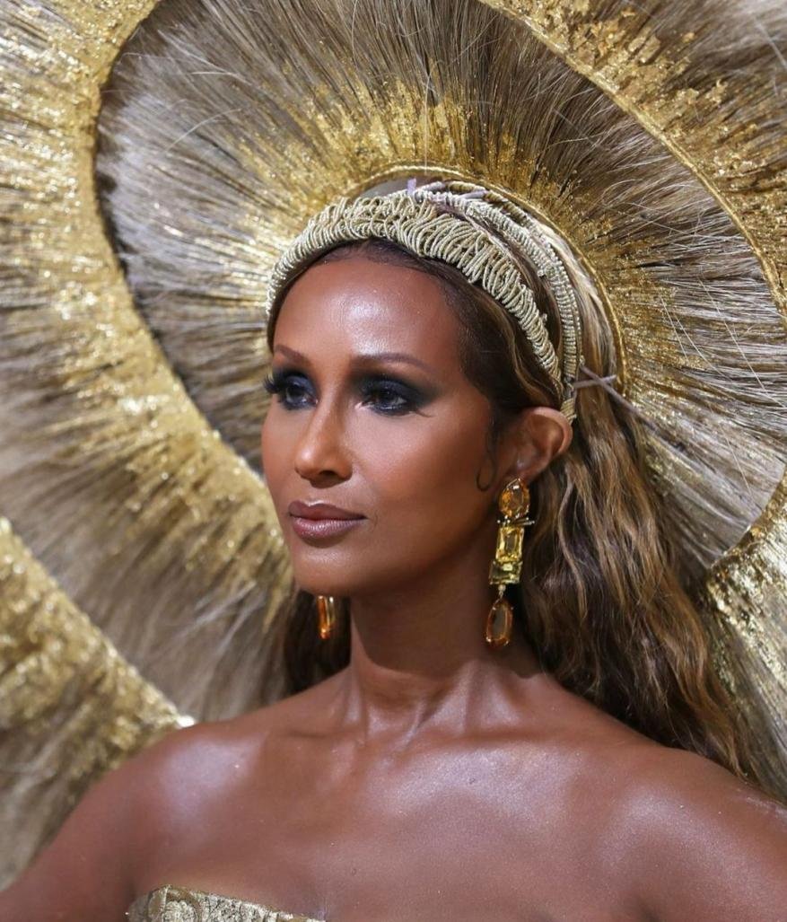 Close-up of a person with tan skin, wearing statement gold earrings, a golden dress and a large golden headpiece. Beauty and fashion concept.