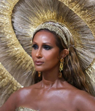 Close-up of a person with tan skin, wearing statement gold earrings, a golden dress and a large golden headpiece. Beauty and fashion concept.