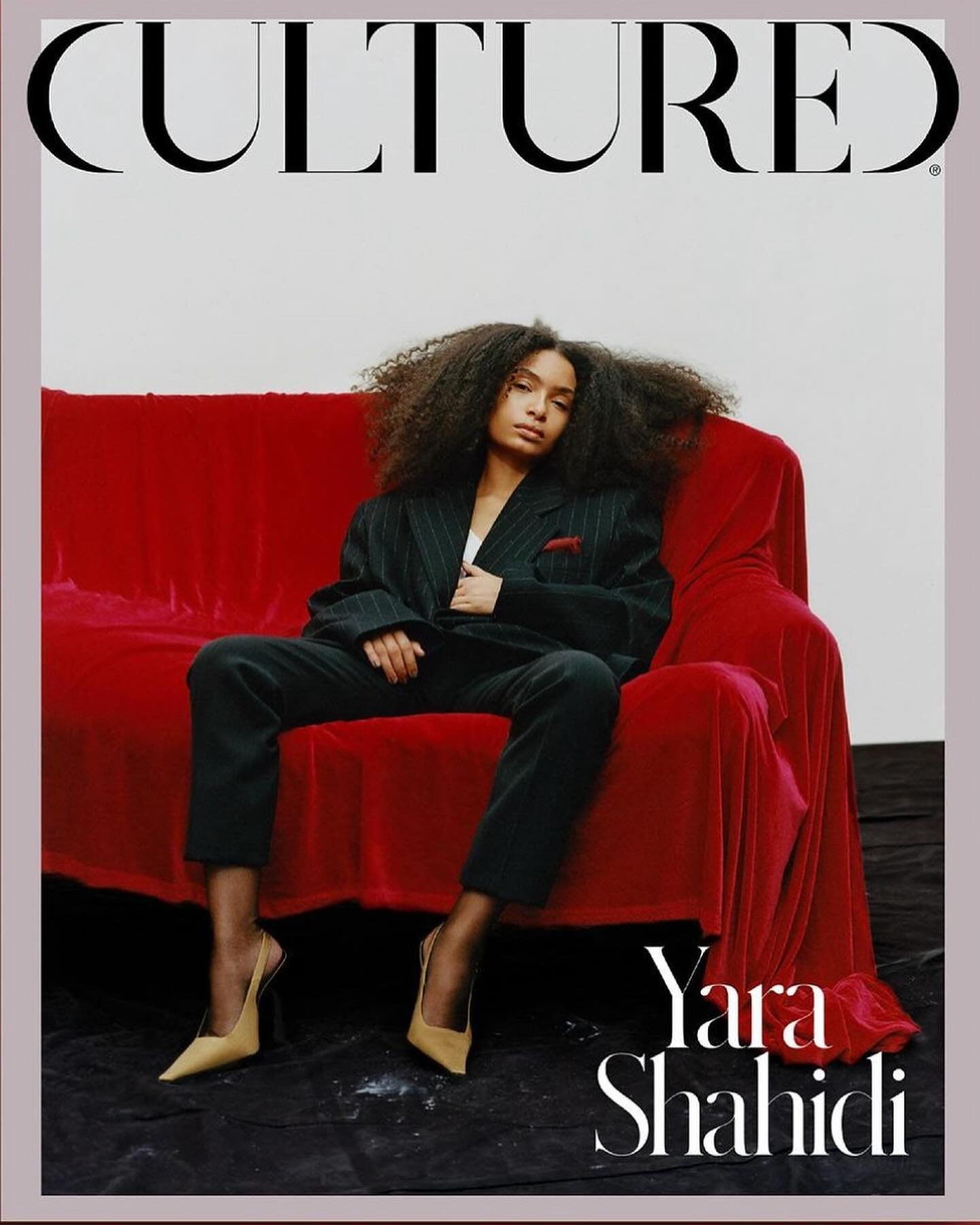 Magazine cover featuring Yara Shahidi sitting on a red velvet couch, wearing a pinstripe suit and nude heels against a neutral backdrop.