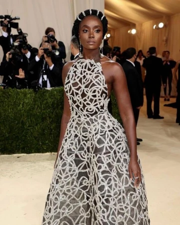 Elegant Black woman on red carpet in elaborate silver gown with braided updo poses at celebrity event with photographers in background.