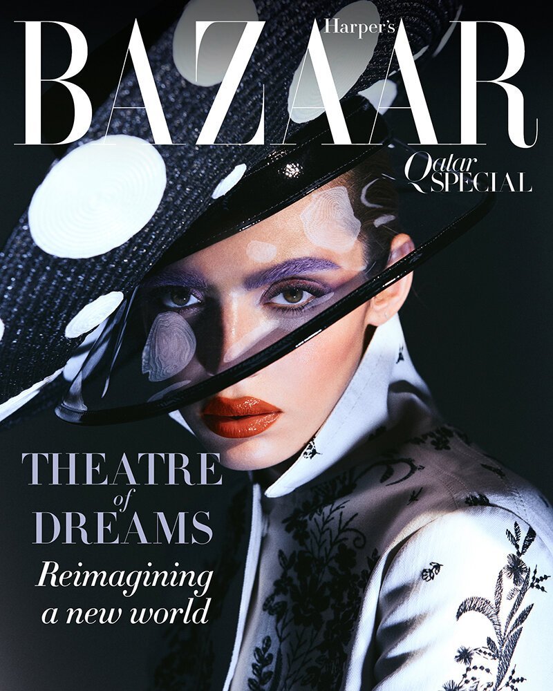 Magazine cover portrait of a woman wearing a large polka dot hat and patterned white jacket with bold purple eye makeup.