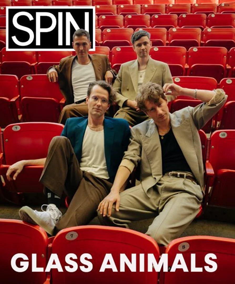 The band Glass Animals poses in an auditorium with red seating for a promotional photo; the band's name and SPIN logo are displayed.