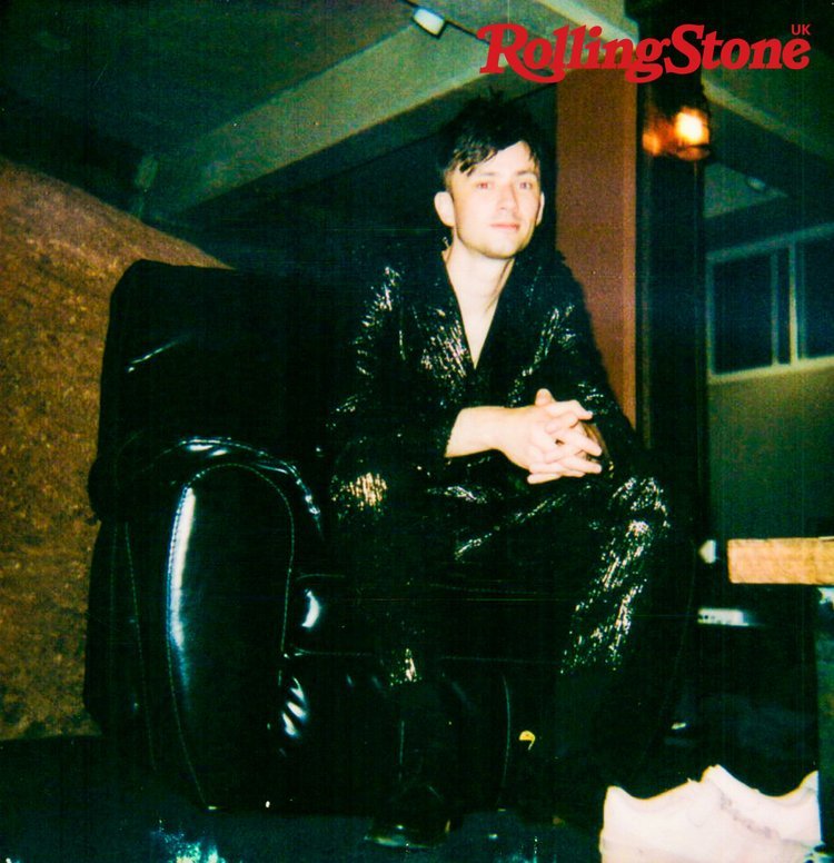 Adult male poses in a black armchair wearing a black sparkly robe in an indoor location with 'Rolling Stone' magazine logo at top.