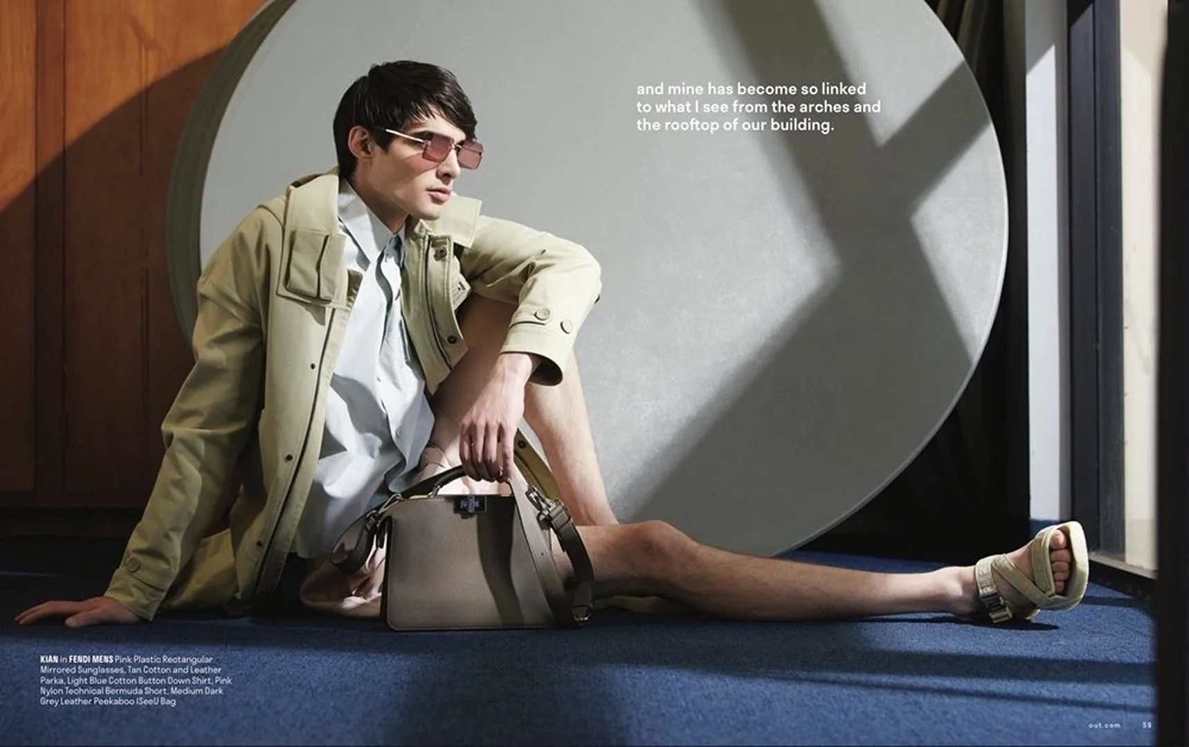 Fashion shot of a stylish adult male model with sunglasses, light jacket, shorts, sandals, bag, seated against a geometric backdrop.