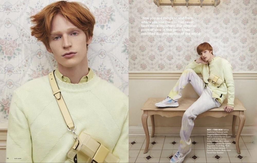 Fashion editorial featuring a young adult male model wearing a light yellow sweater and carrying a bag, posing against a floral wallpaper.