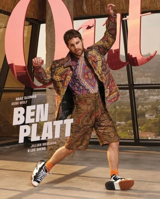 Editorial fashion shot featuring Ben Platt in patterned jacket and shorts, black and white shoes, striking a dynamic pose on a rooftop.