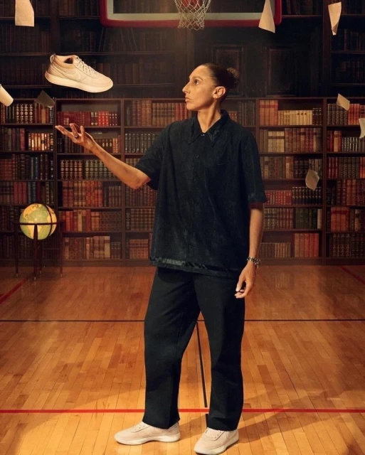 Professional female basketball player wearing casual clothing indoors, juggling a sneaker in the air inside of a basketball court library.