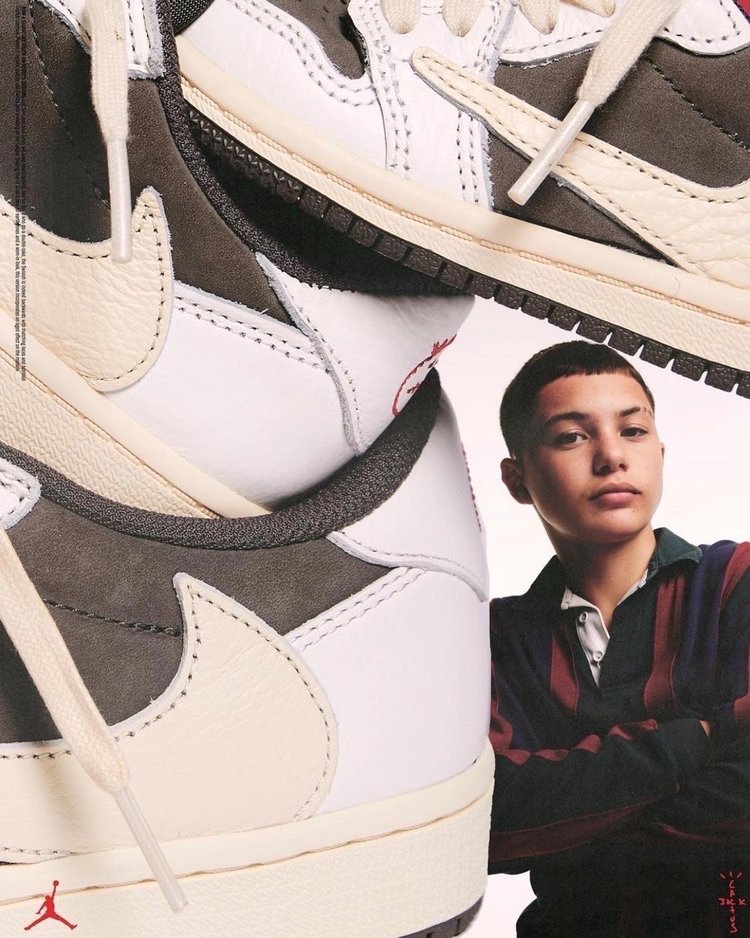 Air Jordan 1 Low OG shoes in white, grey, and beige, featured in a studio product shot with a model wearing a striped polo shirt.
