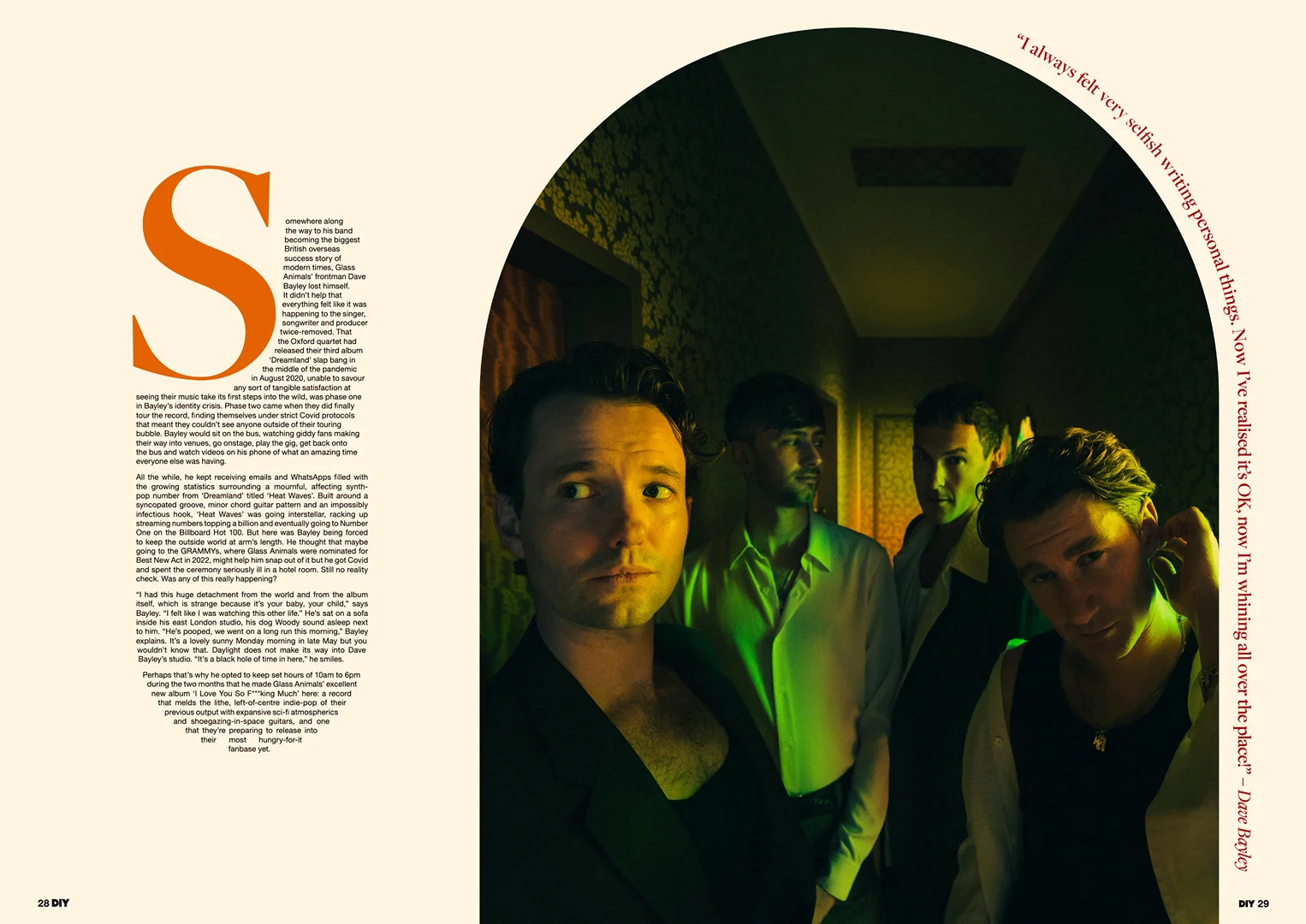 Four men stand in a brightly lit corridor, posing for a stylish editorial shot. The image emphasizes fashion and contemporary aesthetics.