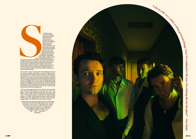Four men stand in a brightly lit corridor, posing for a stylish editorial shot. The image emphasizes fashion and contemporary aesthetics.