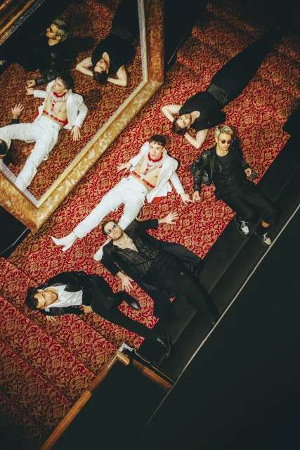 Group of seven people, male and female, wearing formal attire, laying on an patterned floor, shot from a high angle.