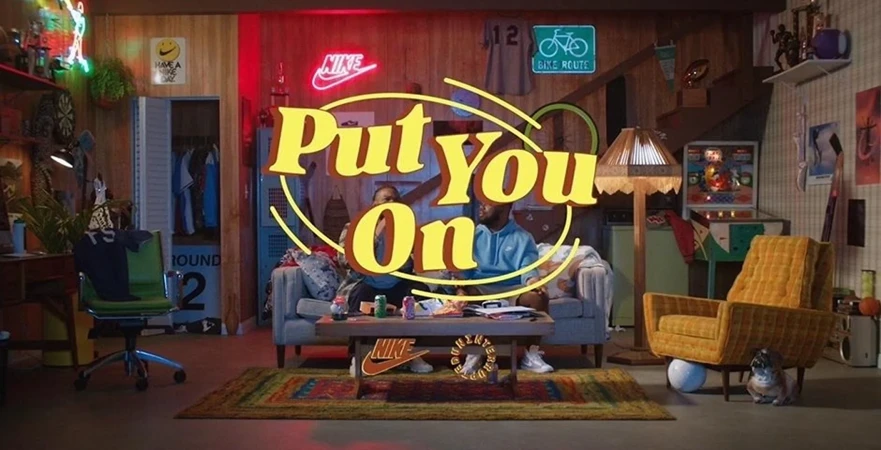 Two adults relaxing on a couch, surrounded by playful retro decor, neon signs, and a whimsical collection of curated objects and props.