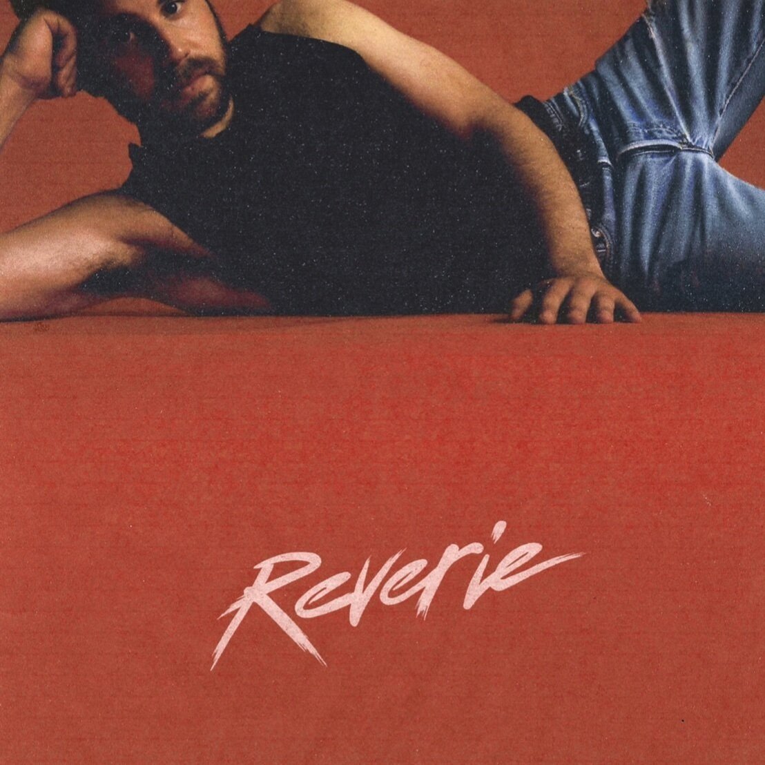 Album cover with a man in jeans and a black t-shirt lying on a red surface with the word 'Reverie' written in white script.