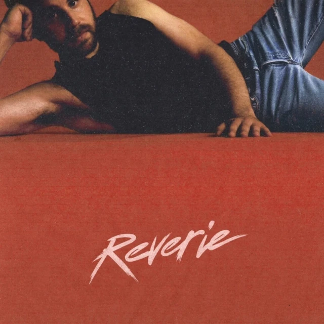 Album cover with a man in jeans and a black t-shirt lying on a red surface with the word 'Reverie' written in white script.