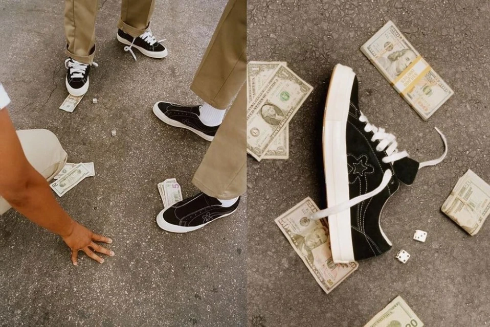 Ground-level shot of black sneakers, dice, and scattered US currency, highlighting street style and urban fashion elements on cracked asphalt.