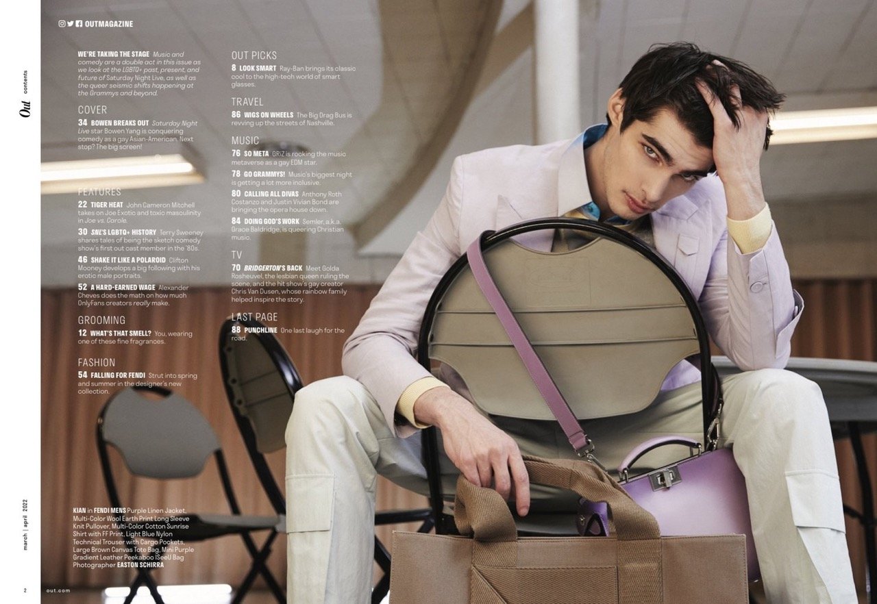 Fashion editorial shot of a young man in a lilac suit sitting on a chair with a tote bag and a lavender handbag in a studio setting.