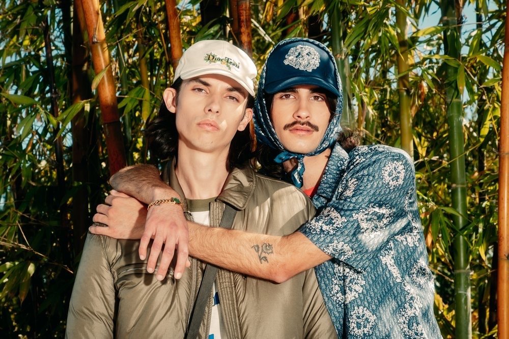 Two male models posing together outdoors in front of a dense bamboo thicket, styled by Kenn Law.