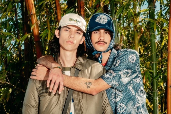 Two male models posing together outdoors in front of a dense bamboo thicket, styled by Kenn Law.